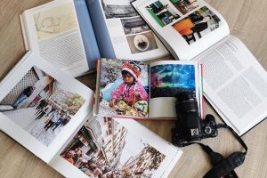 Enkele opengeslagen boeken, waaronder fotoboeken, en een spiegelreflexcamera liggen op een tafel.