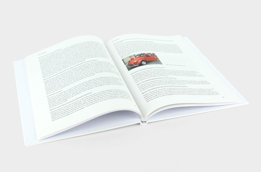 Het hardcover boek Opa vertelt opengeslagen op pagina's met tekst en een foto van een rode Citroën 2CV