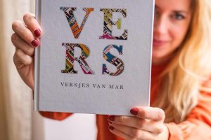 Vrouw met oranje blouse houdt het boek Versjes van Mar vast.