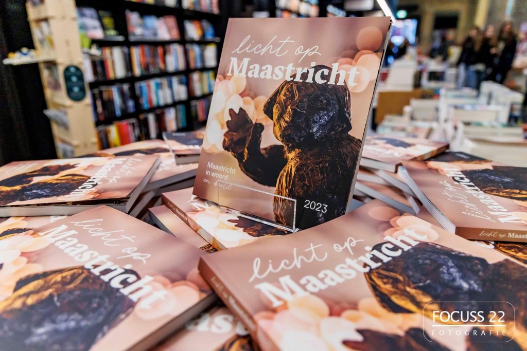Het boek Licht op Maastricht in een boekenstandaard met daaromheen allemaal plat liggende boeken van Licht op Maastricht
